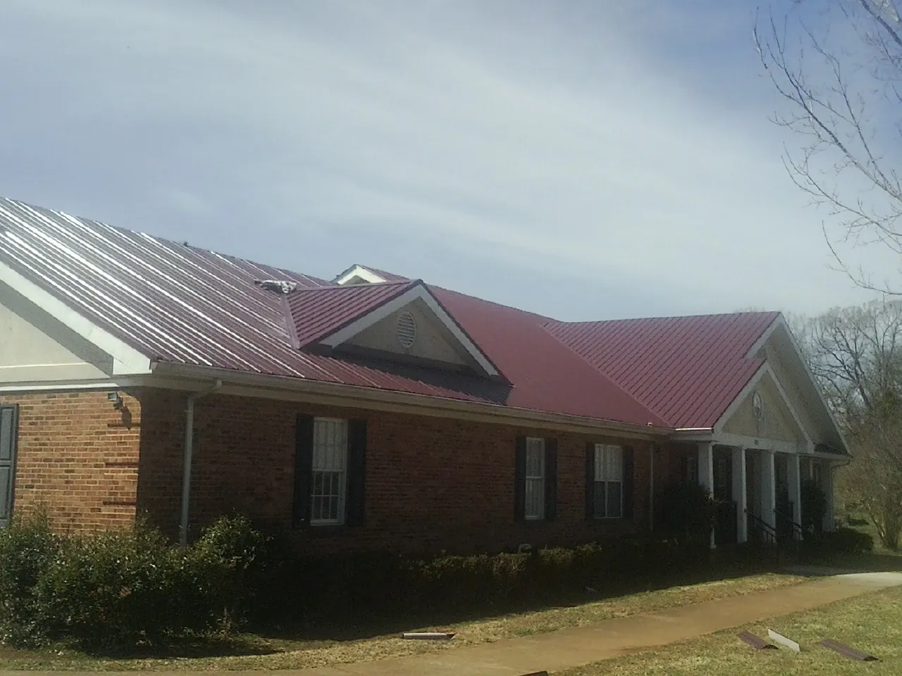 Red metal roof with gabled entries on a long brick building, from a Hail Damage Roof Repair job in Chehalis