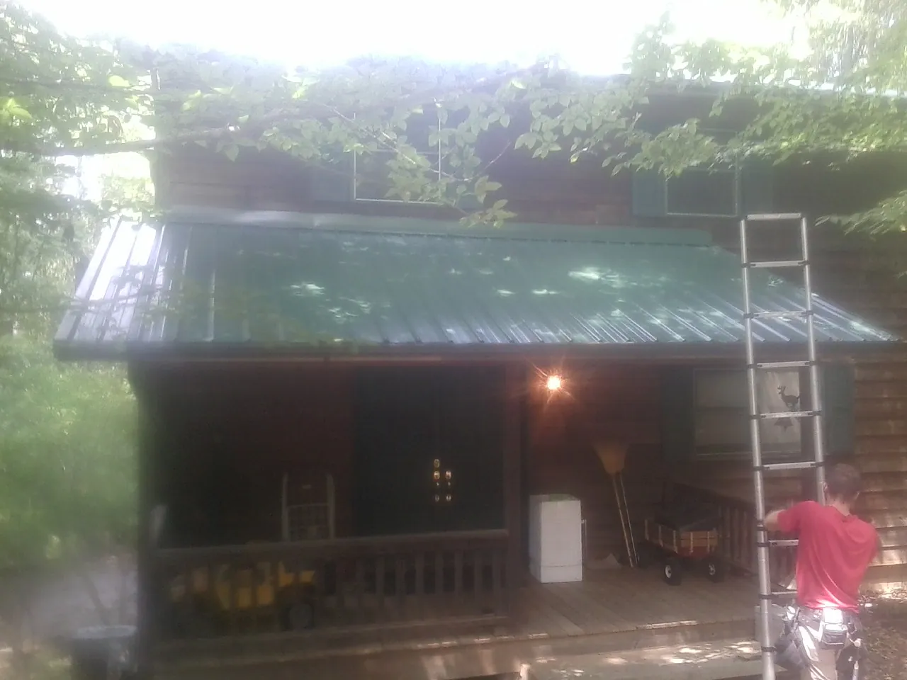 Worker on a ladder at the green porch roof of a wooded cabin in Chehalis