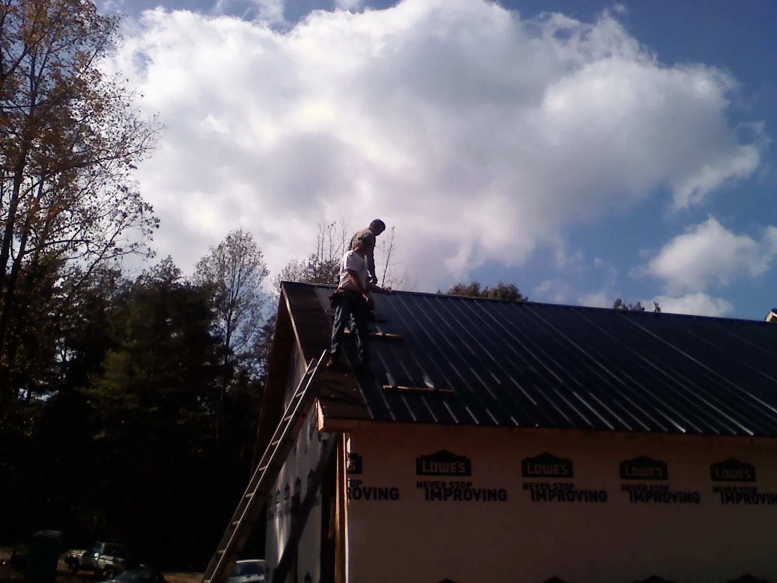 Roofer fastening dark metal panels high against a cloudy sky, from a Roof Inspection job in Chehalis