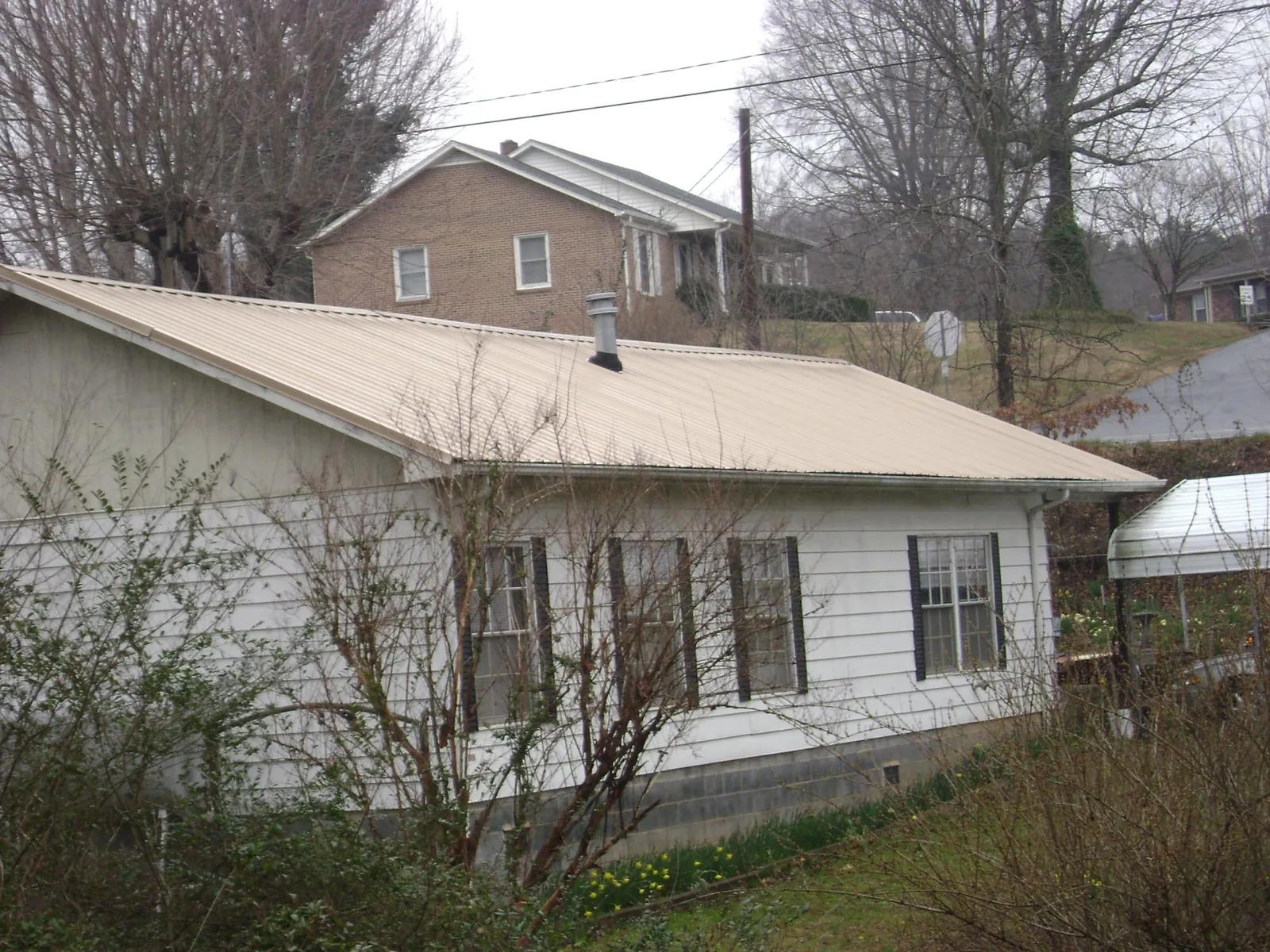 Tan metal roof on a white sided house set into a hillside — Commercial Roofing by Roofing Brothers in Chehalis